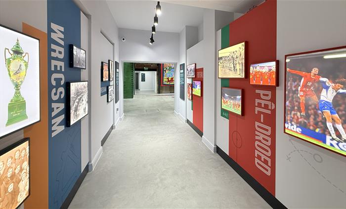 Photo of a white corridor with illuminated photographs of historic local and football scenes and objects on the walls, blue and red features with Wrec